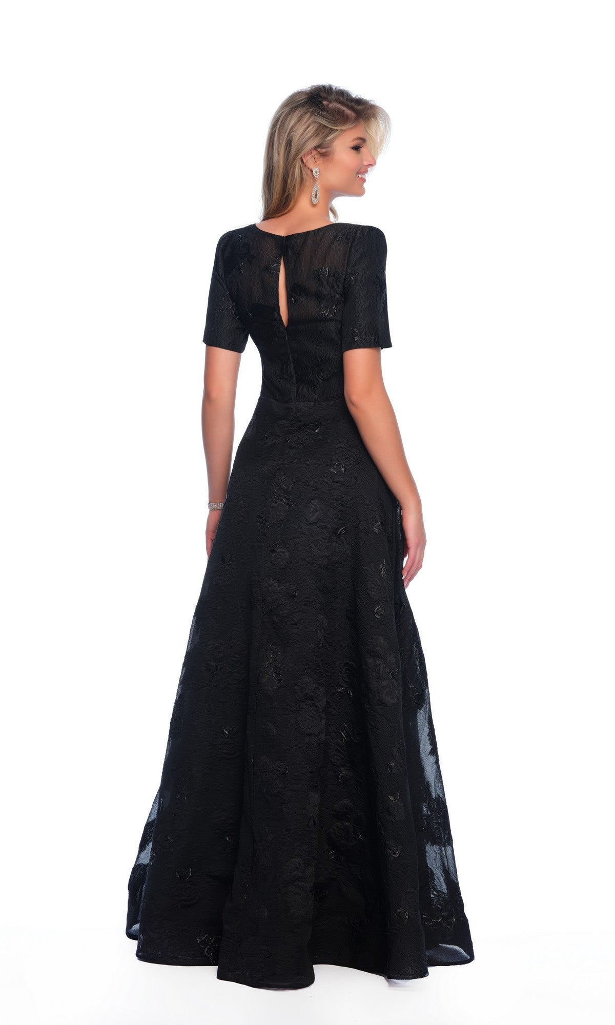 A woman is shown from the back against a white background, wearing the Dave and Johnny 11815 modest black prom dress—floor-length with short sleeves and a subtle textured pattern.